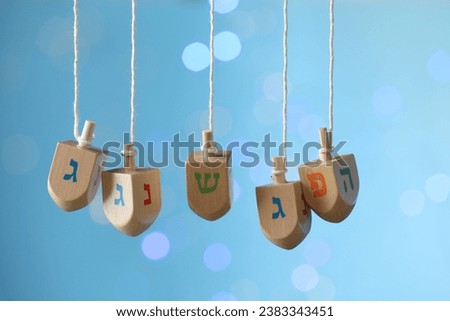 Hanukkah celebration. Wooden dreidels with jewish letters hanging on twine against light blue background with blurred lights Royalty-Free Stock Photo #2383343451