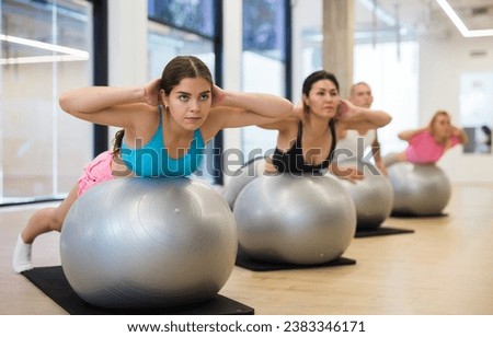 Adult sports people practiciting Pilates in the studio during a group training session perform an exercise on a fitness ball, ..which strengthens the lumbar region and develops overall flexibility Royalty-Free Stock Photo #2383346171