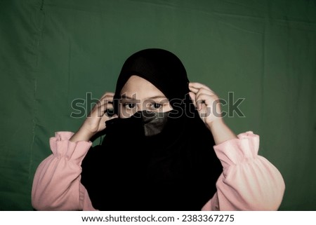 A southeast Asian girl wearing a black hijab and wearing a black health mask