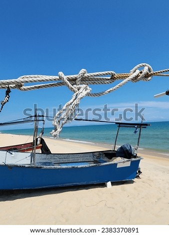 The picture shows a fishing boat stranded on the seashore. The boat rope is visible in front. The picture was taken at noon.