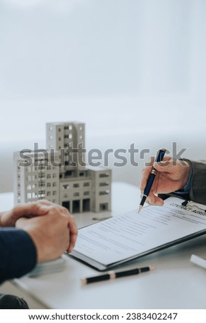 Close-up photo of a real estate agent offering a contract to purchase or rent a residence. Businessman holds small house model with property insurance at table in home sales office