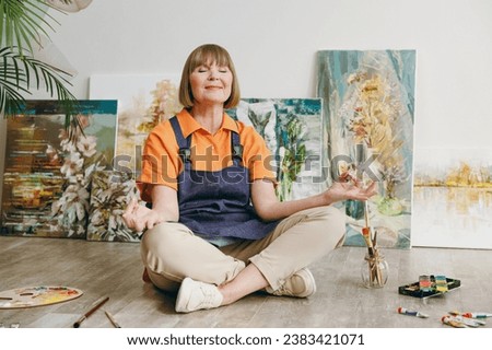 Full body elderly artist woman 50 years old wears casual clothes stand near easel with painting hold spread hands in yoga om gesture spend free spare time in living room indoor. Leisure hobby concept