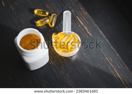 Omega 3 fish oil yellow capsules in a plastic measuring spoon, dietary supplement on dark wooden board, healthy eating concept, close up view.