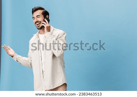 Portrait of a man brunette animation and joy talking on the phone smile with teeth, on a blue background in a white T-shirt and jeans, copy space
