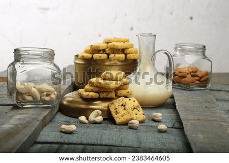 Rich butter cashew cookies, cashew jars, and a jug of melted butter placed side by side on wooden surfaces, isolated against a backdrop. High Resolution
