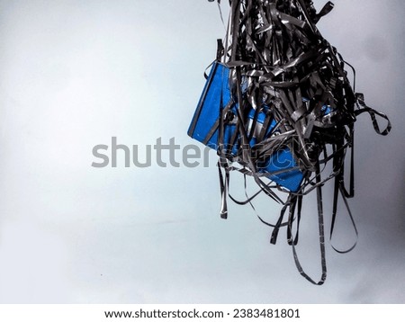 A broken old blue cassette cassette tape wrapped around its ribbon and dangling on a white background
