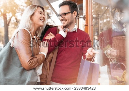 Attractive young married couple spending weekend together shopping for clothes and presents. Two people smiling outdoors and looking at each other.