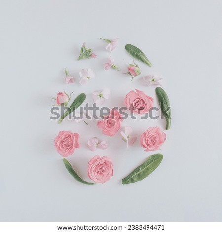 An abstract Easter egg made out of green leaves, pink rose petals and white flowers on the pastel background.  Aesthetic composition. Decorative arrangement.