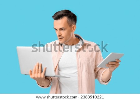 Handsome man with laptop and tablet computer on blue background