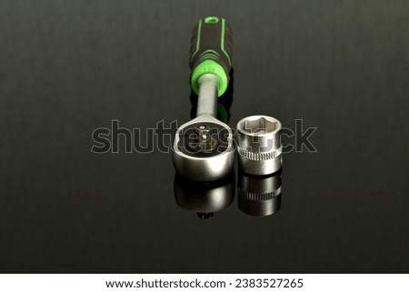 On the black surface of the table lies a locksmith's ratchet wrench, with a green handle and one removable head. Royalty-Free Stock Photo #2383527265