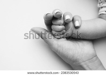 Parents' hands hold the fingers of a newborn baby. The hand of a mother and father close-up holds the fist of a newborn baby. Family health and medical care. Tiny fingers in a black and white photo.
