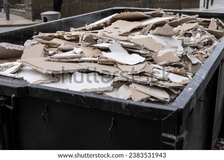 an overloaded dumpster waste container, with construction waste and drywall plasterboard, debris generated during the reconstruction process. Royalty-Free Stock Photo #2383531943