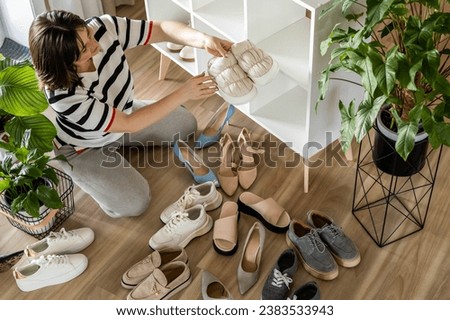 Woman arrangement sneakers on shoes closet shelf comfortable storage organizing method at home. Female footwear cupboard organize neatly folded boots seasonal wardrobe cleaning and maintaining Royalty-Free Stock Photo #2383533943