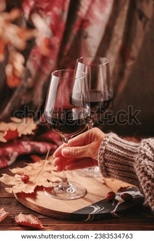 Autumn still life with two glasses of red wine and dry leaves in rustic style on dark wooden background. Womans hand holding glass. Romantic sweater weather, wine tasting concept