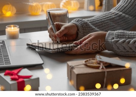 Young woman writing christmas cards, makes order on laptop. Female picking gifts online purchases at cozy home among gift boxes and packages. Winter sales, Black Friday. Christmas discount promotions