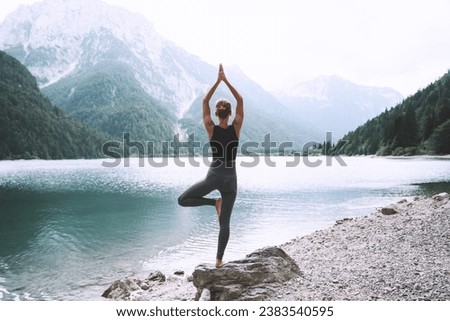 Young woman is practicing yoga at mountain lake. Girl doing yoga on nature. Healthy lifestyles. Concept of vitality, balance, mindfulness, zen energy, calmness, relaxation. Royalty-Free Stock Photo #2383540595