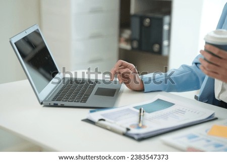 Asian and African businesswoman using laptop and drinking coffee in modern office