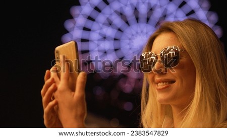 Happy woman enjoy neon light evening. Beautiful sun glasses reflection. Cool fun amusement park. Blond girl smile close up. Dark city night. Joy inspiration face. Person take selfie mobile phone shoot
