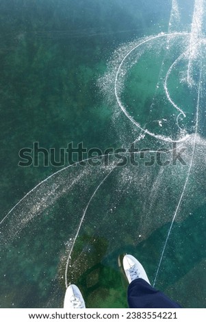 Skating on a frozen lake on a sunny winter day. Top view of beautiful thin transparent ice of frozen Baikal Lake and white figure skates. Winter travel and active recreation. Abstract ice background