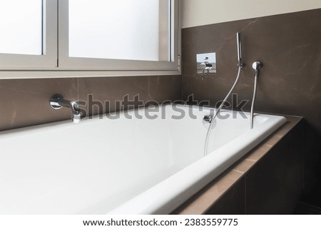 Close-up of a white bathtub in a minimalist bathroom with brown tiles