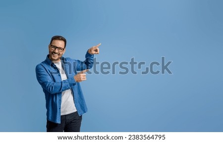 Portrait of smiling businessman pointing at copy space for advertising isolated on blue background