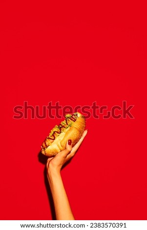 Hand holding hot tasty American hotdog with beef sausage, sauces with green salad against vivid red background. Concept of fast food, street food, delivery. Copy space for text Royalty-Free Stock Photo #2383570391