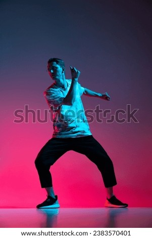 Active lifestyle. Vertical portrait of dynamic hip-hop dancer practising isolated over gradient pink purple background in neon light. Concept of dance, youth, hobby, dynamics, movement, action, ad