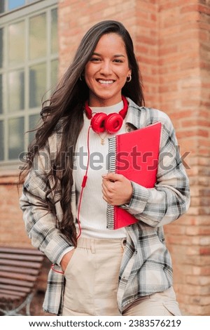Vertical individual portrait of a pretty hispanic female student smiling and looking at camera at high school. Head shot of latin teenage girl standing outdoors at the university campus. Education