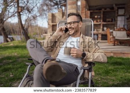 One adult man 40 years old caucasian male sit in front of his house on vacation talk on his smartphone mobile phone call happy smile during the conversation real person copy space Royalty-Free Stock Photo #2383577839