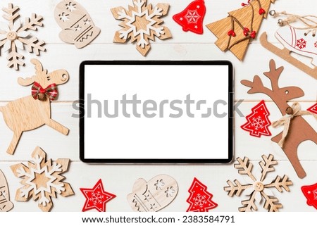 Top view of tablet on holiday wooden background. New Year decorations and toys. Christmas concept.