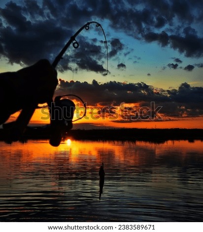 Fishing at sunset. Catching predatory fish on spinning. Sunset colors on the water surface, sunny path from the low sun. Perch caught on yellow spoonbait Royalty-Free Stock Photo #2383589671
