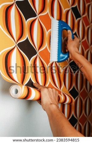 a caucasian man uses a blue brush to attach a geometric patterned wallpaper to a white wall Royalty-Free Stock Photo #2383594815
