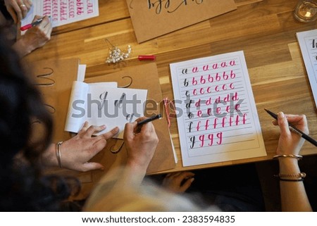 Top view of crop anonymous ladies writing alphabet letters on paper with pencil and brush