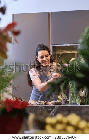 Professional female florist in uniform smiling and looking down while arranging bouquet of blooming flowers during workday in modern floral shop Royalty-Free Stock Photo #2383596407