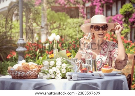Stock photo of happy woman wearing sunglasses drinking a glass of champagne in garden.