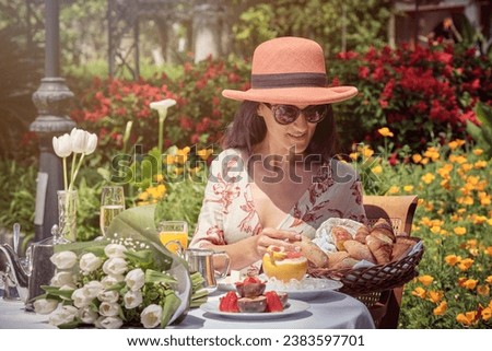 Stock photo of happy woman eating croissants in the garden during sunny day.