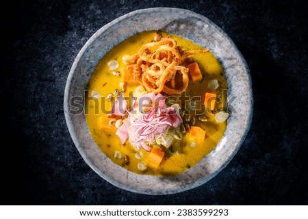 Top view of tasty pumpkin puree soup with fish and fried onion served in bowl on black background in restaurant