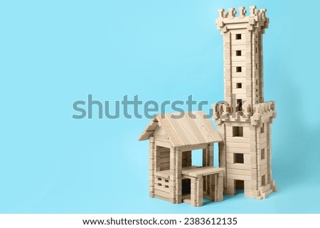 Wooden tower and house on light blue background, space for text. Children's toy