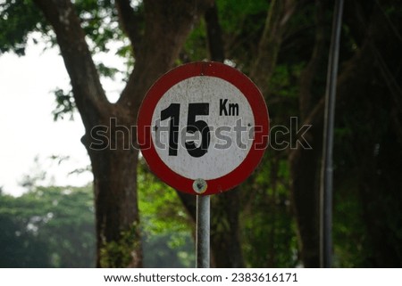 Fifteen kilometers per hour speed limit sign with trees on the background. Maximum speed on the road. Safety on road background. White round sign red border line.