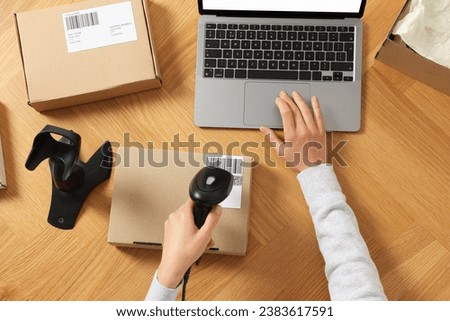 Woman with scanner reading parcel barcode at wooden table, top view. Online store Royalty-Free Stock Photo #2383617591