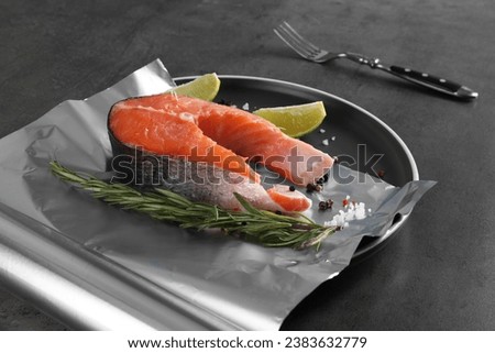 Aluminum foil with raw fish, lime, rosemary and spices on grey table. Baking salmon Royalty-Free Stock Photo #2383632779