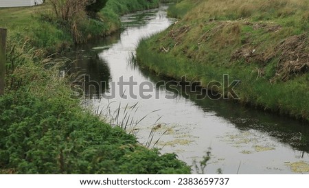 Wide angle view of a bend on a stream, with grass banks either side.