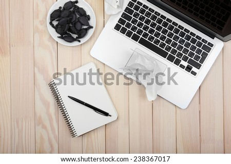 Open notebook and crumbled diary papers with saucer of candies on wooden background, top view