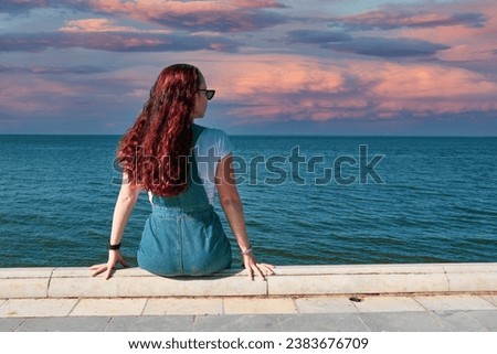 beautiful girl with red hair looks towards the horizon against the background of the sea. High quality photo