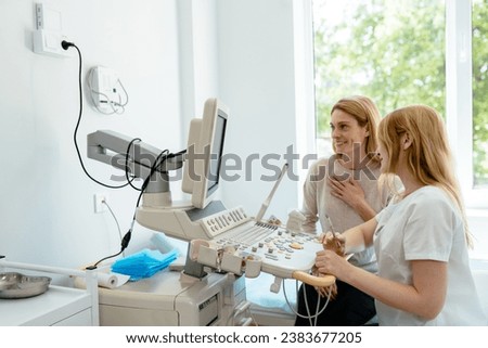 Female doctor showing baby ultrasound picture to pregnant woman. Happy middle age female patient sits next to doctor, communication, smile in medical office.