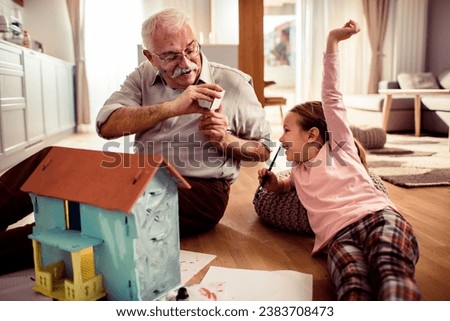 Grandfather taking a picture of his granddaughter while painting a toy house