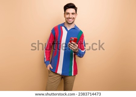 Photo of nice cheerful young man toothy smile hold smart phone chatting isolated on beige color background