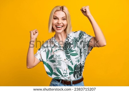 Photo portrait of attractive young woman raise fists celebration dressed stylish leaves print clothes isolated on yellow color background