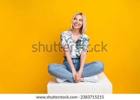 Full length photo of good mood dreamy girl dressed print blouse look at sale empty sit on cube isolated on yellow color background