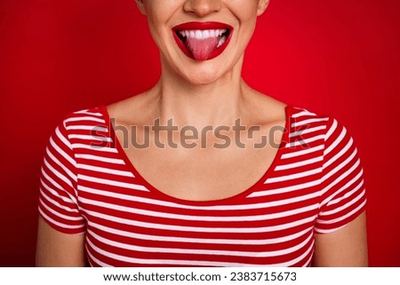 Close up cropped portrait of good mood young funny lady showing tongue protrude wearing striped t shirt isolated on red color background